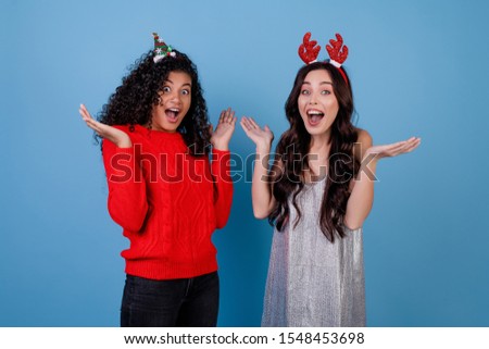 diverse caucasian and black women wearing holiday hoops isolated over blue