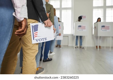 Diverse citizens at ballot station on election day. White and African American male and female voters holding voting forms in hands standing in line at polling place. Crop shot. US democracy concept 