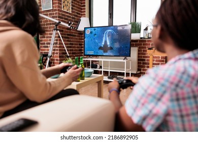 Diverse close friends in living room sitting on sofa while playing space sim videogame on gaming device. People sitting at home while enjoying fun leisure activity with entertainment console device.