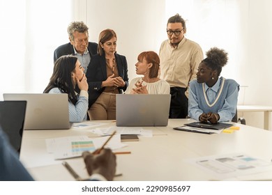Diverse Colleagues Discussing a Project - Multiethnic group, including Caucasians, Americans, Chinese, and Africans, attentively discussing a project in front of a laptop, with a woman presenting. - Powered by Shutterstock