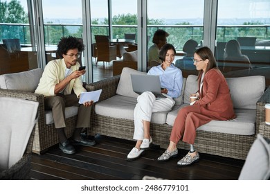 Diverse colleagues enjoy a break on a modern office rooftop terrace, engaging in conversation and work. - Powered by Shutterstock