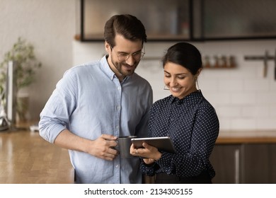 Diverse colleagues standing in kitchen office at lunch break discuss collaborative project use digital tablet. Married couple of business people talk in morning before workday, modern tech app concept