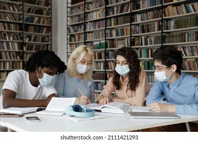 Diverse College Students In Protective Medical Masks Writing Notes, Summary In Public Library, Studying In Group Together, Working On Learning Project, Reading Book, Textbook, Talking