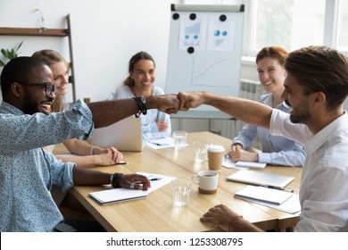 Diverse Company Staff Girls Guys Sitting At Desk In Boardroom Feel Happy And Satisfied Celebrating Success At Work. Diverse Colleagues Fist Bumping Greeting Each Other Express Friendship And Respect