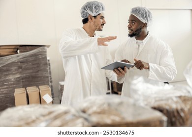 Diverse controller with tablet talking to black blue collar worker at food factory.