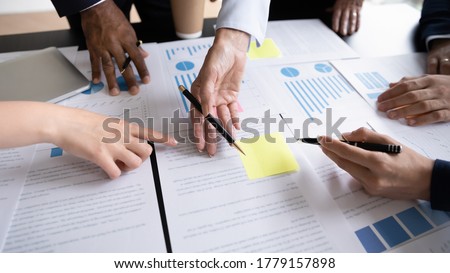 Diverse corporate staff discuss report shown in charts and graphs, analyzing financial stats, involved in project overview, reviewing results, close up. Employees participate in brainstorming concept