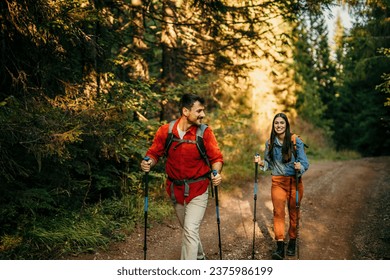 A diverse couple with backpacks and hiking poles eagerly explore the great outdoors, reveling in the serenity and beauty of their surroundings - Powered by Shutterstock