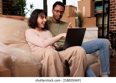 Diverse Couple Doing Online Shopping On Laptop To Buy Furniture, Browsing Internet Website For Home Decor Inspiration. Moving In Rented Apartment Property Together For Relationship Event.