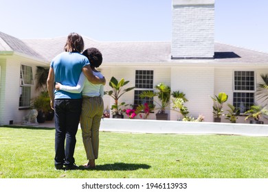 Diverse Couple Embracing In Front Of House On Sunny Garden Terrace. Staying At Home In Isolation During Quarantine Lockdown.