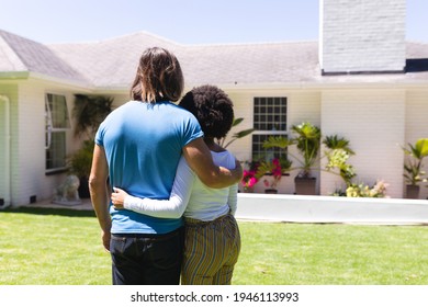 Diverse Couple Embracing In Front Of House On Sunny Garden Terrace. Staying At Home In Isolation During Quarantine Lockdown.