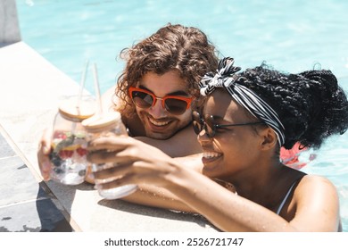 Diverse couple enjoying drinks by the pool, the woman hair adorned with a headband. Their cheerful mood and summer attire suggest a relaxing vacation vibe. - Powered by Shutterstock