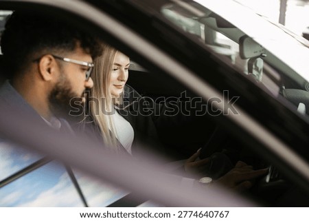 Diverse couple exploring car features and technology inside a vehicle at a modern automotive showroom, considering buying