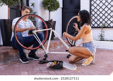 Diverse couple fixing bicycle together outdoors. They are in outdoor courtyard with potted plants and brick steps, working as a team, unaltered - Powered by Shutterstock