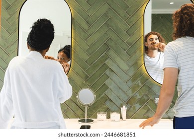 A diverse couple is grooming and brushing teeth in a bright bathroom. The African American woman applies makeup, while her Caucasian partner brushes his teeth, unaltered. - Powered by Shutterstock