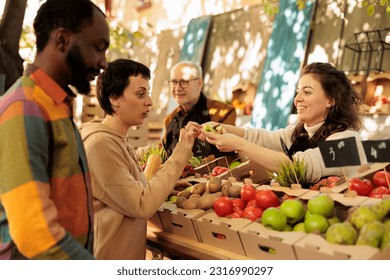 Diverse couple man and woman buying fresh natural produce at farmers market, looking at bio products. Smiling local vendor standing behind fruits and vegetables stand, sell healthy food. - Powered by Shutterstock