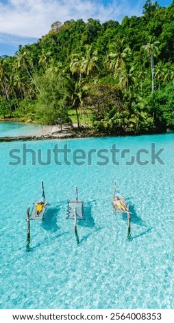A diverse couple of man and woman in a hammock in the ocean Lush greenery surrounds them, capturing the tranquil beauty of Koh Kood, Thailand.