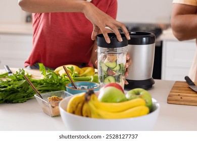 Diverse couple preparing smoothie together in kitchen. Fresh fruits and vegetables are on the counter, creating a healthy and vibrant atmosphere, unaltered - Powered by Shutterstock