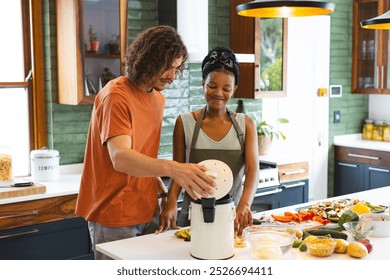 A diverse couple is putting food waste in compost bin together in the kitchen. The Caucasian man and African American woman, both young, are using a blender amid various fresh ingredients, unaltered - Powered by Shutterstock