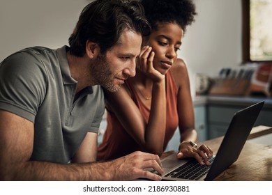 Diverse Couple Searching For A New Rental Apartment Home On Their Laptop Sitting Together In Their Kitchen At Their House. Man And Woman In An Interracial Marriage Relationship Doing Online Shopping