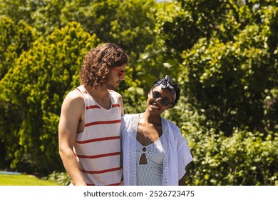 A diverse couple shares sunny day in garden. A young Caucasian man with brown hair and a young African American woman with short black hair and sunglasses enjoy a joyful moment - Powered by Shutterstock