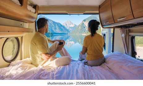 A diverse couple sits in a campervan, enjoying coffee and the breathtaking view of a Norwegian fjord from their window. a diverse man and women in a mobile home lovatnet lake Lodal Valley Norway - Powered by Shutterstock