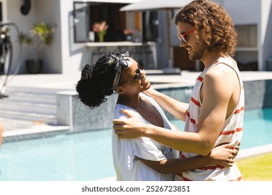 Diverse couple: Young African American woman and Caucasian man embrace by a pool. She wears a headscarf and sunglasses; he sports curly hair and red-striped tank top. - Powered by Shutterstock