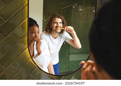 Diverse couple, young African American woman and young Caucasian man brush their teeth together. They are reflected in a bathroom mirror, highlighting a shared routine in a domestic setting. - Powered by Shutterstock