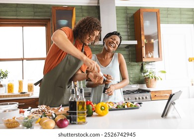 Diverse couple, young African American woman and Caucasian man laugh while cooking together. Surrounded by fresh vegetables in a bright kitchen, they share a joyful moment preparing a meal. - Powered by Shutterstock