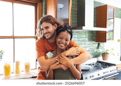 Diverse couple young Caucasian man embraces a young African American woman in a sunny kitchen. Both are smiling, wearing casual clothes, conveying a sense of warmth and affection. - Powered by Shutterstock