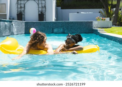 Diverse couple young Caucasian man and African American woman relax on a yellow float in a pool. They enjoy a sunny day outdoors, creating a leisurely and intimate atmosphere. - Powered by Shutterstock