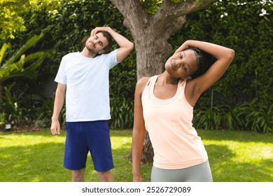 Diverse couple, a young Caucasian man and African American woman, stretch in a sunny backyard. Both wear casual sportswear, enjoying a fitness routine outdoors. - Powered by Shutterstock