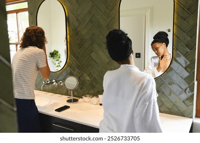 Diverse couple: young Caucasian man and African American woman stand by a bathroom sink. He is in a striped shirt, she wears a white robe, both engaged in morning routines. - Powered by Shutterstock