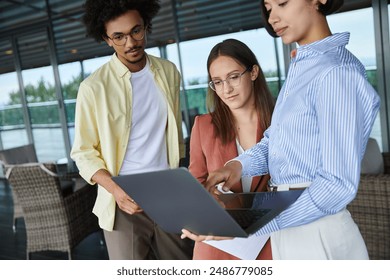 Diverse coworkers chat on a rooftop terrace, sharing a laptop and ideas. - Powered by Shutterstock