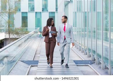 Diverse Coworkers Going Down Urban Footpath Outside. Business Man And Woman Walking Near Office, Using Tablet And Talking. Conversation Outdoors Concept