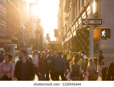 Diverse Crowd Of Anonymous People Walking Down A Busy Street In Manhattan, New York City With Bright Sunlight Shining In The Background