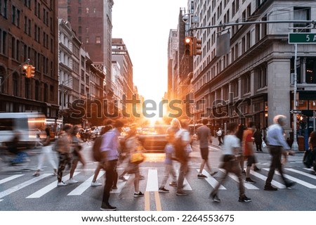 Diverse crowds of people walking through a busy intersection on 5th Avenue and 23rd Street in New York City with sunset in background