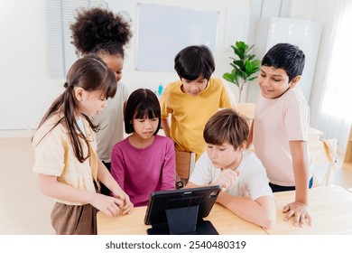 Diverse elementary students collaborate on digital tablet in modern classroom. Multicultural group engages in interactive learning, showcasing inclusive education and technological integration - Powered by Shutterstock