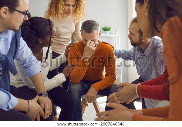 Diverse empathetic people in group therapy\
session comforting mature man going through difficult life period.\
Team of patients sharing problems and helping each other deal with\
grief or addiction