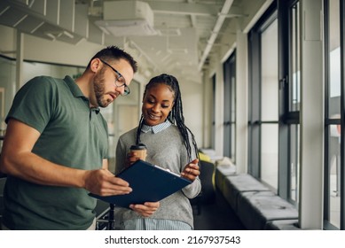 Diverse employees standing in modern office and chatting during break while discussing project or sharing news. Caucasian businessman and African American businesswoman having pleasant conversation. - Powered by Shutterstock