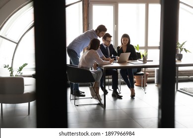Diverse employees team with leader wearing glasses working together in modern boardroom behind glass wall, colleagues looking at laptop screen, discussing project statistics, sharing ideas