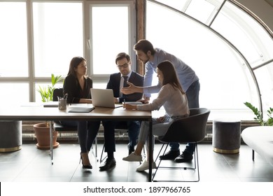Diverse employees with team leader working together, using laptop, sitting at table in modern office, confident mentor coach training staff, colleagues discussing online project, sharing ideas - Shutterstock ID 1897966765