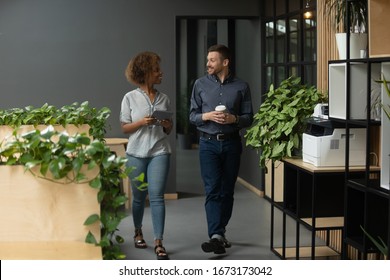 Diverse employees walking in modern office, chatting during break, discussing project or sharing news, Caucasian businessman and African American businesswoman having pleasant conversation