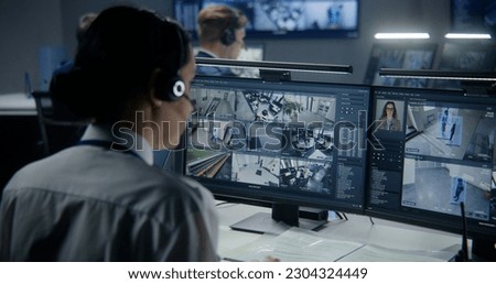 Diverse employees work in security control center, watch CCTV cameras with AI face scanning. Female operator uses PC. Computer monitors and big digital screens with surveillance cameras video footage.