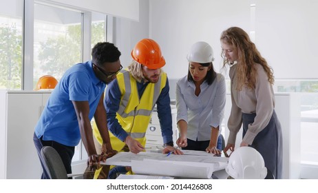 Diverse engineering team meeting to discuss architectural project and smiling at camera. Multiethnic construction designers working on blueprint at table in office and looking at camera