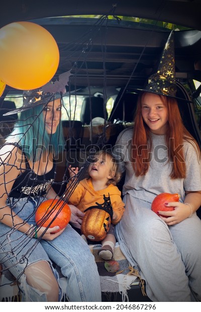 Diverse family friends celebrating Halloween in\
car trunk outdoors