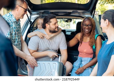 Diverse Family And Friends Loading Trolley In Automobile Trunk, Preparing To Leave On Holiday Trip. Travelling By Car On Summer Vacation, Going To Seaside Destination With Multiethnic People.