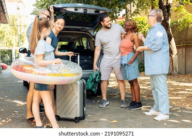 Diverse Family And Friends Travelling On Holiday, Preparing To Leave On Summer Vacation And Loading Baggage In Car Trunk. People Sitting In Driveway To Go To Seaside Adventure Trip.