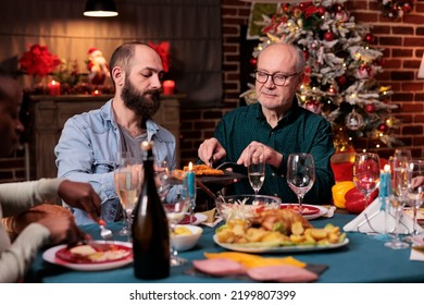 Diverse Family Having Christmas Festive Dinner, Eating Traditional Food At Decorated Table, Man Holding Plate, Passing Dish. People Gathering With Parents On Xmas Holiday