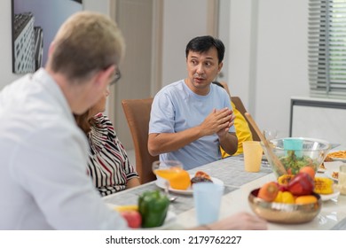 Diverse Family Meeting And Having Dinner Together Sitting At The Table At Home. Caucasian Couple Visiting Relatives. People Enjoy Talking While Eating Food.