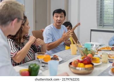 Diverse Family Meeting And Having Dinner Together Sitting At The Table At Home. Caucasian Couple Visiting Relatives. People Enjoy Talking While Eating Food.